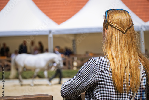 Blonde woman is watching a horse exhibition 