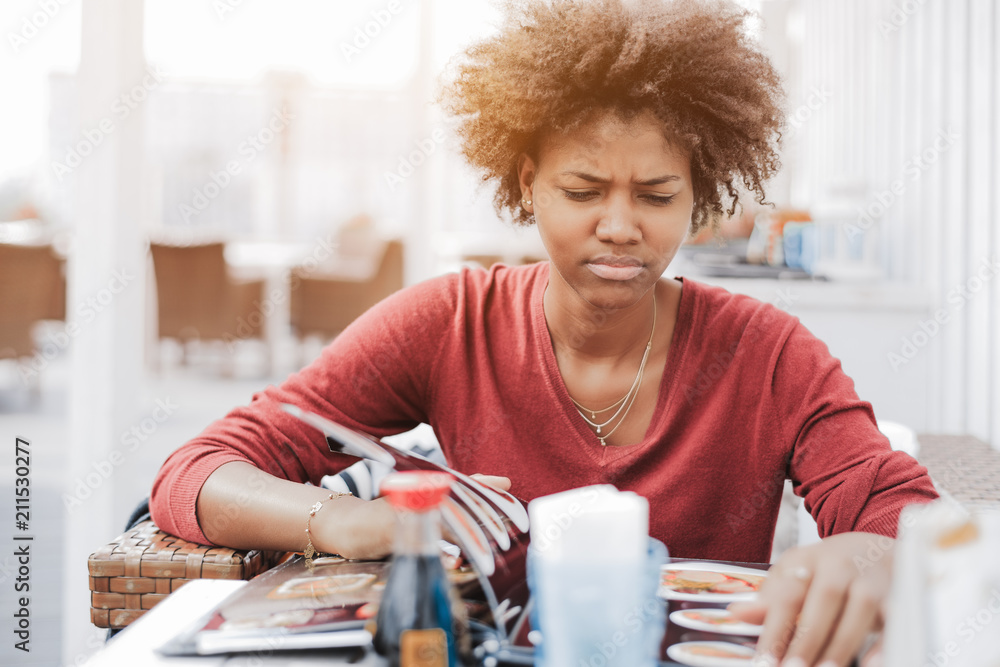 Wall Mural Cute curly African-American girl in street cafe is dissatisfied with an assortme