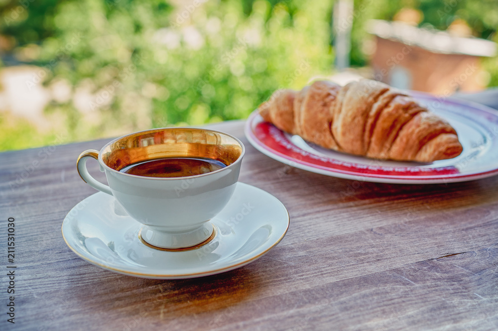 Coffee cup and croissant on wooden table in green garden Coffee cup and croissant on wooden table in green garden