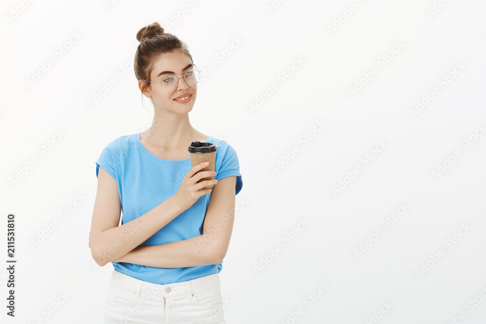 Great day to be productive. Good-looking feminine female in glasses and bun hairstyle, looking right with sensual smile, holding cup of coffee, having break during lunch at work over grey wall Great day to be productive. Good-looking feminine female in glasses and bun hairstyle, looking right with sensual smile, holding cup of coffee, having break during lunch at work over grey wall