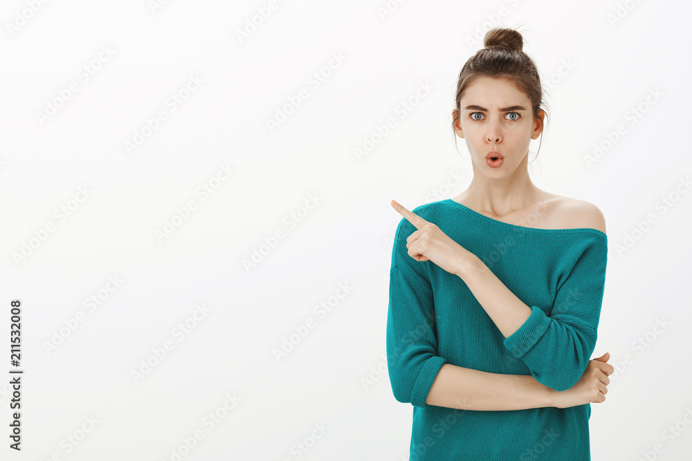 Shock, look there. Portrait of stunned displeased charming woman in green loose sweater, frowning and folding lips while pointing at upper left corner, expressing dislike and negative attitude Shock, look there. Portrait of stunned displeased charming woman in green loose sweater, frowning and folding lips while pointing at upper left corner, expressing dislike and negative attitude