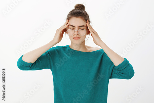 Just a sec, headache again. Portrait of intense gloomy and tired woman in casual outfit and glasses, closing eyes, touching temples and frowning while suffering migraine or painful feeling