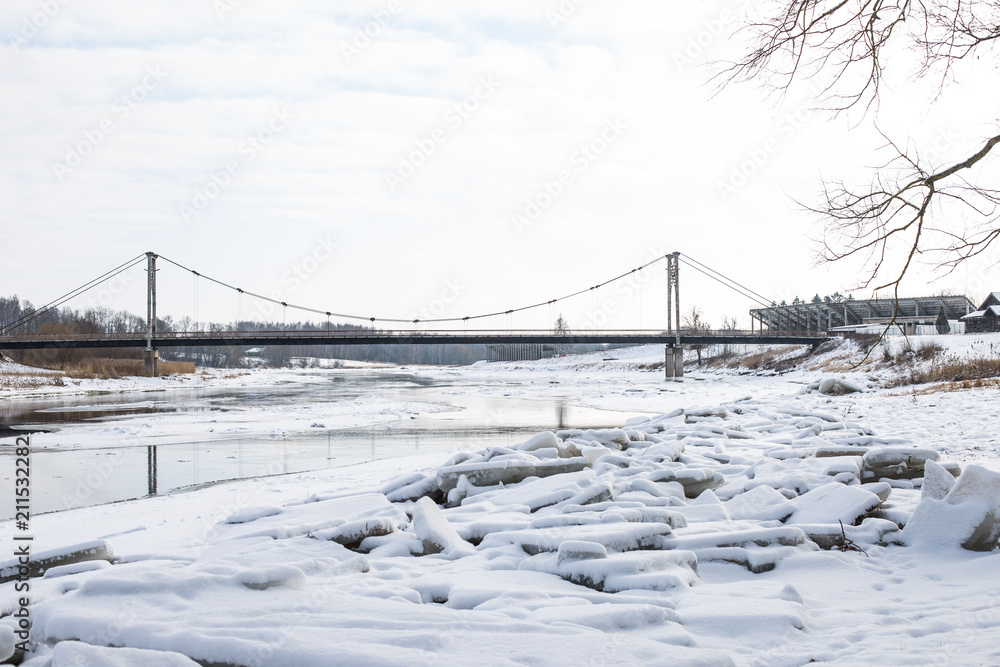 Snowed river with big ice cubes on the shores. .Cableway bridge across the river.  Winter theme.