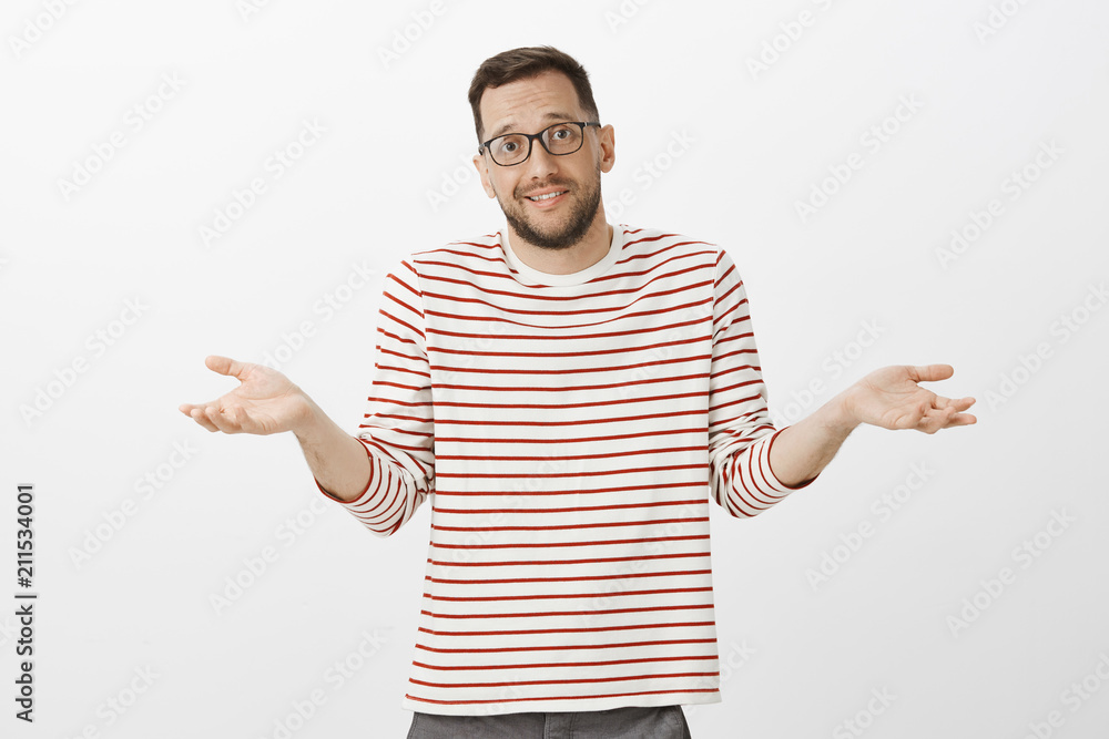 Portrait of clueless unaware handsome guy in glasses, shrugging with spread palms and awkward expression, being confused and questioned, having no idea about question over gray background Portrait of clueless unaware handsome guy in glasses, shrugging with spread palms and awkward expression, being confused and questioned, having no idea about question over gray background