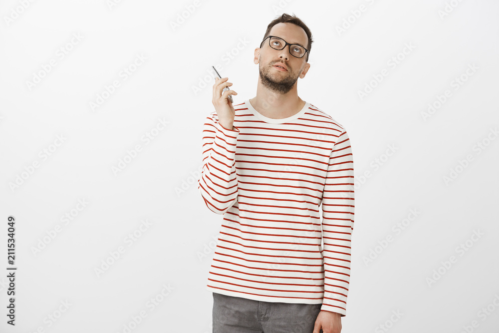 Hate hanging on phone. Bothered annoyed attractive european man in glasses, looking up bored and holding smartphone near ear as if being fed up with uninteresting talk, standing over gray wall Hate hanging on phone. Bothered annoyed attractive european man in glasses, looking up bored and holding smartphone near ear as if being fed up with uninteresting talk, standing over gray wall