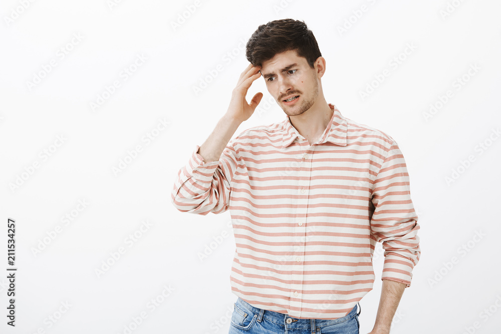 Guy trying to recall what he forgot. Portrait of forgetful confused attractive man with beard and moustache, looking down and holding palm on temple, feeling nervous while thinking over gray wall Guy trying to recall what he forgot. Portrait of forgetful confused attractive man with beard and moustache, looking down and holding palm on temple, feeling nervous while thinking over gray wall