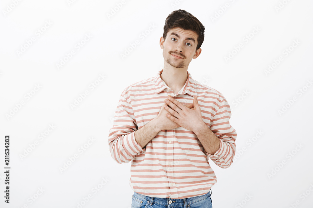 Studio shot of indifferent sarcastic european man with moustache, smirking and holding palms over heart, imitating pleasure and thankful attitude, standing against gray background Studio shot of indifferent sarcastic european man with moustache, smirking and holding palms over heart, imitating pleasure and thankful attitude, standing against gray background