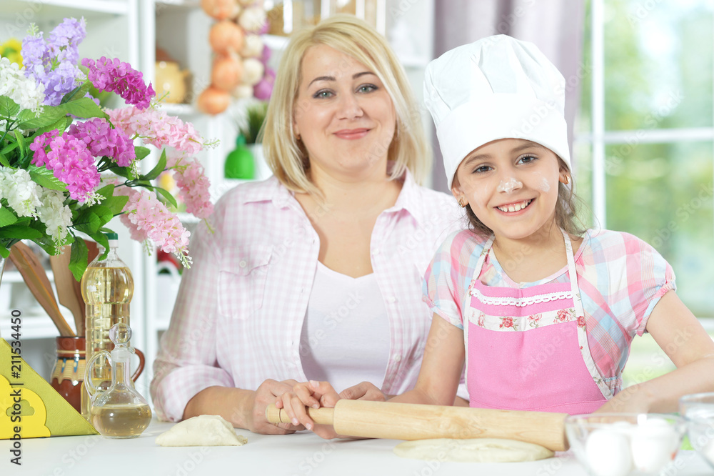 Cute girl in white hat with her mother making dough Cute girl in white hat with her mother making dough