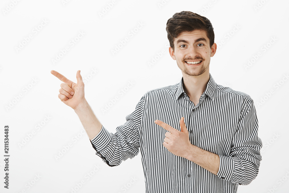 Portrait of flirty funny european male model with moustache and beard in striped shirt, pointing left with finger gun gestures and smiling broadly, inving cute woman to continue talking in bar Portrait of flirty funny european male model with moustache and beard in striped shirt, pointing left with finger gun gestures and smiling broadly, inving cute woman to continue talking in bar