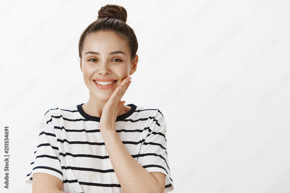Girl is pleased with result of beauity therapy. Charming healthy european woman in striped t-shirt, touching cheek gently, smiling broadly and being happy to receive compliments over white wall Girl is pleased with result of beauity therapy. Charming healthy european woman in striped t-shirt, touching cheek gently, smiling broadly and being happy to receive compliments over white wall