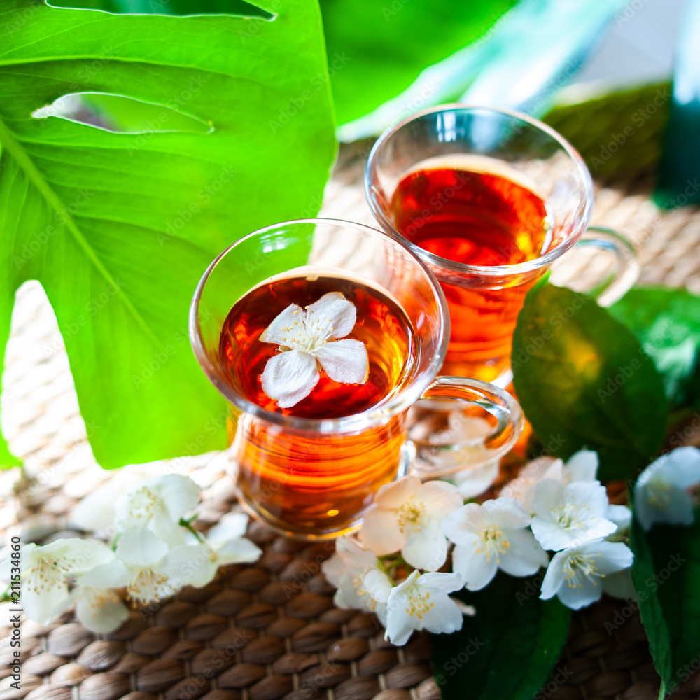 Tea with jasmine. Two cups of tea on a natural background of green leaves with jasmine flowers. Tea with jasmine. Two cups of tea on a natural background of green leaves with jasmine flowers.