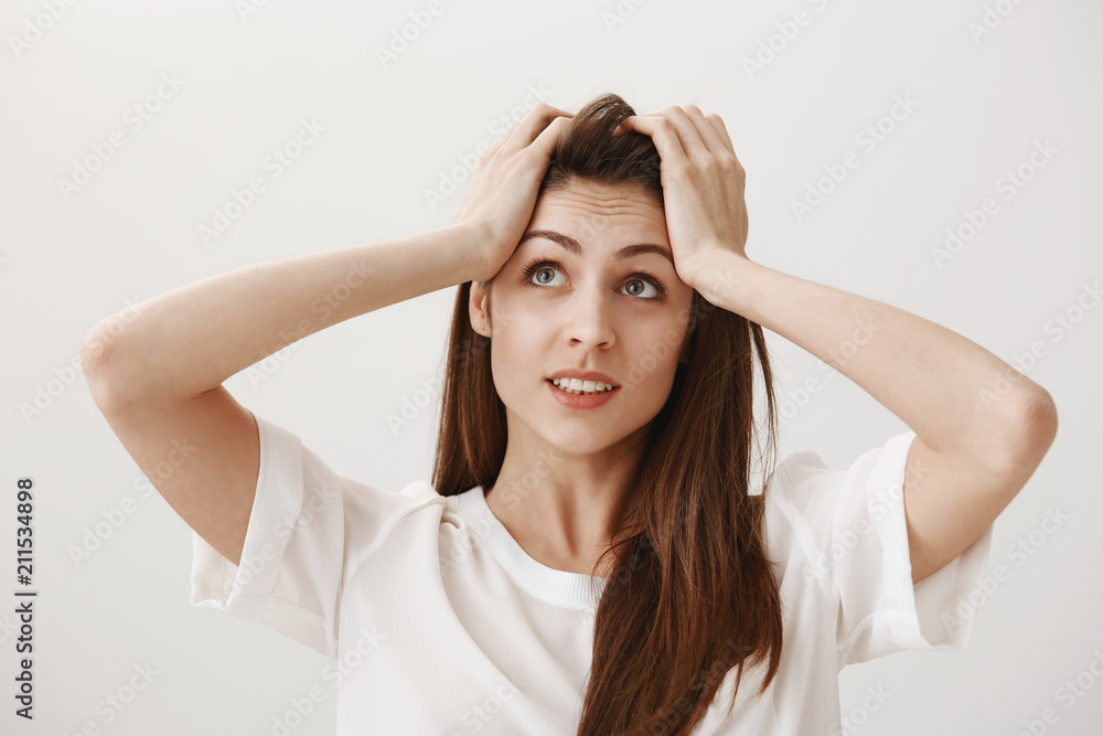 Deadline coming closer. Portrait of worried and pressured attractive young female looking at clock on wall and holding hands on forehead, being in hurry and late on meeting, worried over gray wall Deadline coming closer. Portrait of worried and pressured attractive young female looking at clock on wall and holding hands on forehead, being in hurry and late on meeting, worried over gray wall