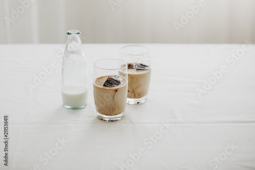 Frozen coffee ice cubes in a glass poured with milk to make a refreshing summer iced coffee drink. White background, isolated, copy space.