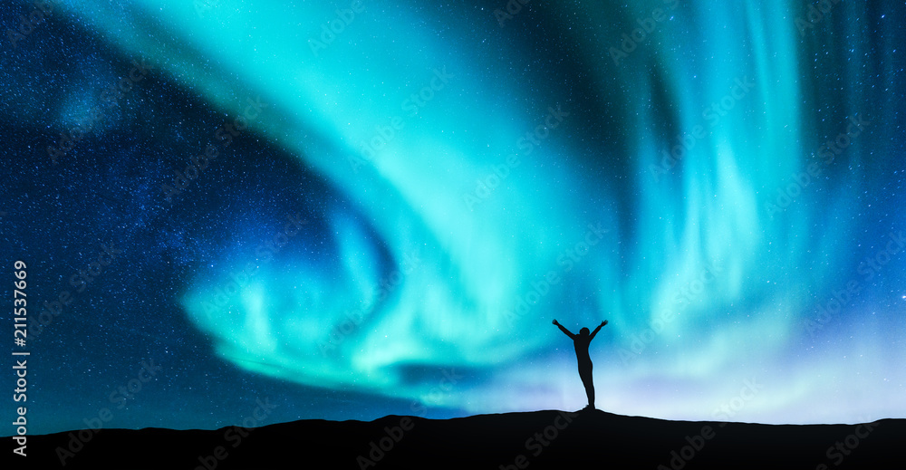 Northern lights and silhouette of standing woman with raised up arms on the  hill in Norway. Aurora borealis and happy girl. Starry sky, green polar  lights. Night landscape. Travel background. Concept Stock