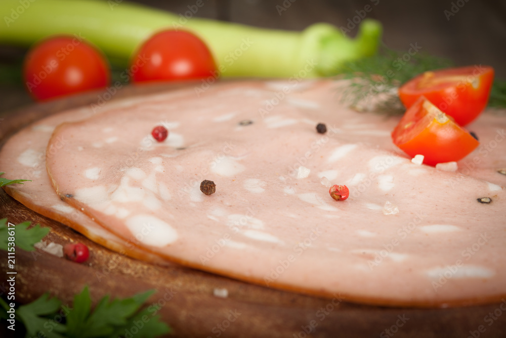 Italian mortadella salami on wooden board with tomato and green pepper