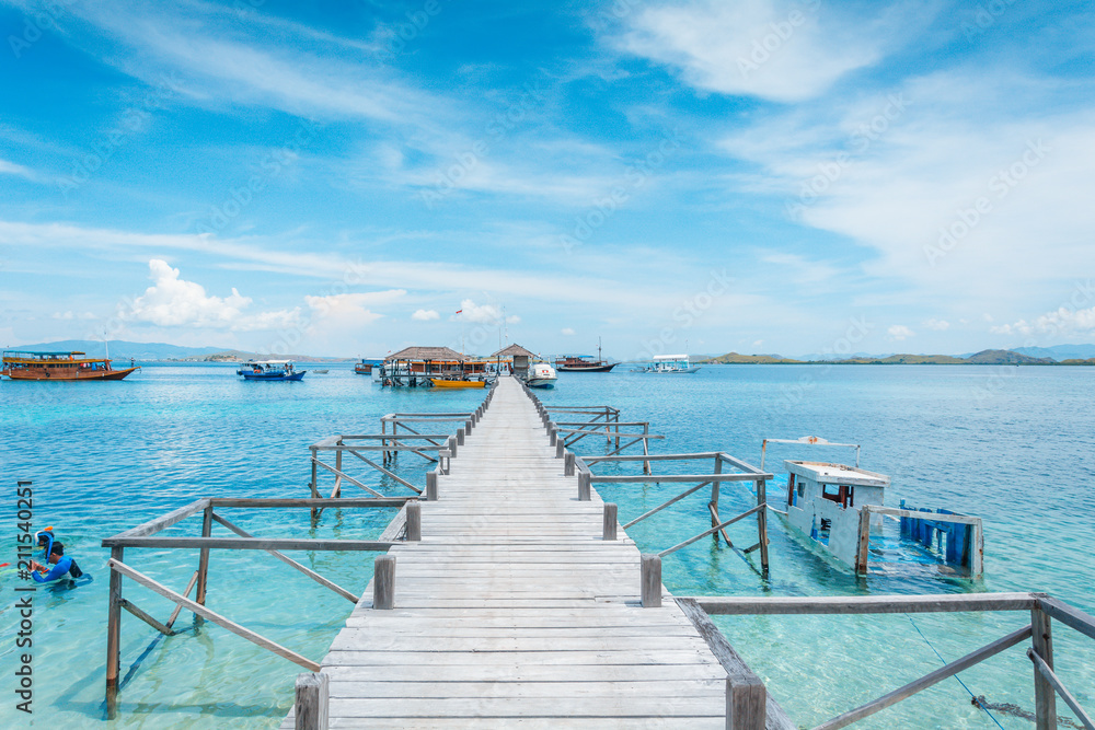 View of the wooden pier from the coast of Kanawa Island with turquoise sea and tourist boats, Komodo Island (Komodo National Park), Labuan Bajo, Flores, Indonesia