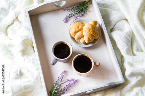 Croissants and coffee on a wooden white tray with lavender flowers in bed. Romantic breakfast. Top view photo