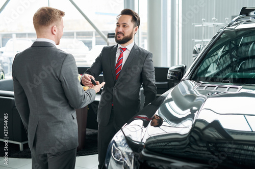Salesman passing key to businessman in auto at dealership