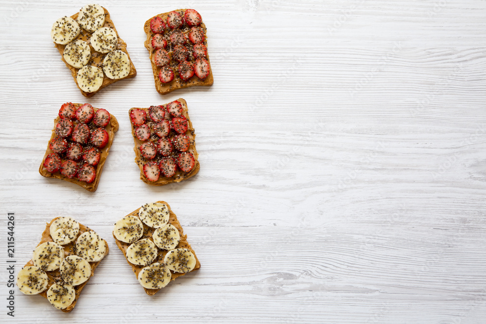 Vegetarian toasts with peanut butter, fruits and chia seeds on a white wooden table, from above. Dieting concept. Copy space. Vegetarian toasts with peanut butter, fruits and chia seeds on a white wooden table, from above. Dieting concept. Copy space.