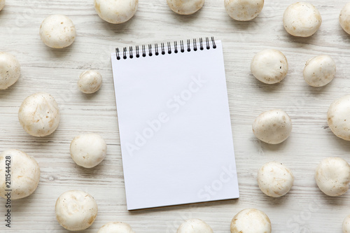 Champignon mushrooms with notepad over white wooden background, top view. From above.