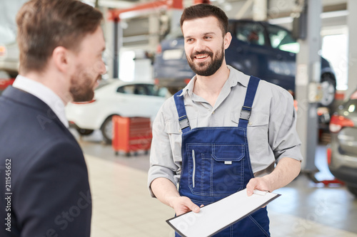 Waist up portrait of smiling  bearded mechanic talking to businessman standing in clean modern car service and repair center
