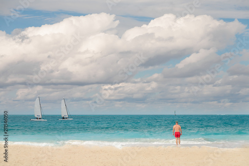 Tableau sur toile Man in red shorts looks out onto the tropical water