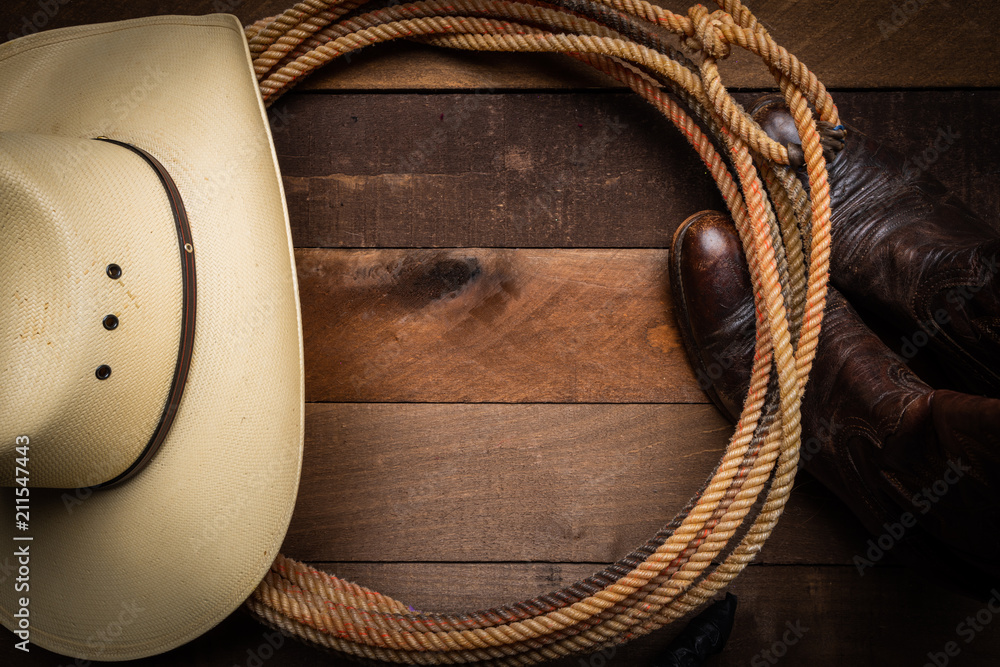 A cowboy hat, lariat rope and boots on a wooden plank background