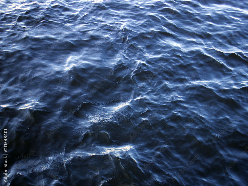 Blue water surface, light waves with sun flares, may be used as background or texture