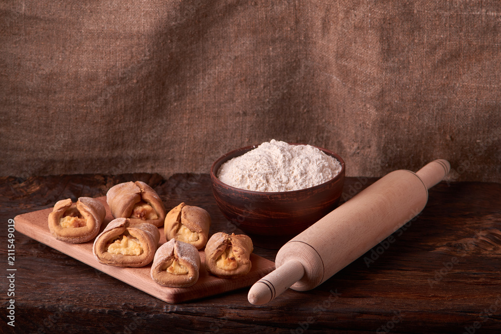 Fototapeta premium Composition of tasty cottage chees cookies on chopping board with bowl flour and rolling pin. on rustic background