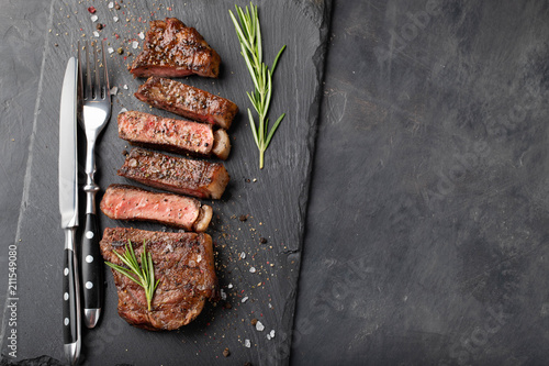 Closeup ready to eat steak new York beef breeds of black Angus with herbs, garlic and butter on a stone Board. The finished dish for dinner on a dark stone background. Top view with copy space photo