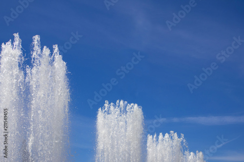 Tops of large fountain jets gushing upwards against blue sky  may be used as background