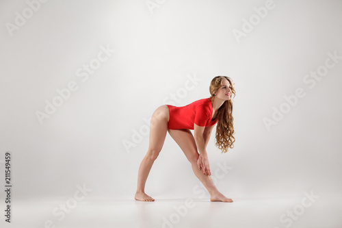 attractive athletic woman in red leotard doing yoga pose isolated on white studio background.