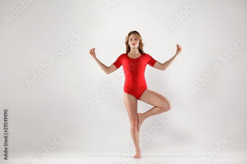 attractive woman in red leotard standing on one leg and doing tree yoga pose
