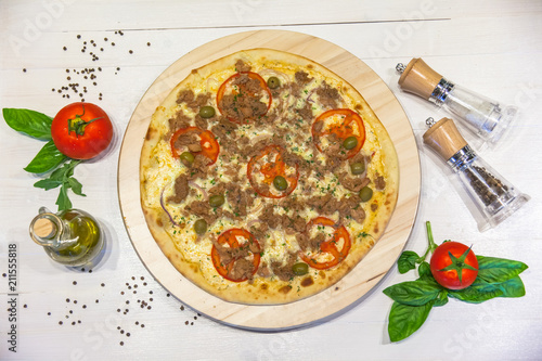 appetizing pizza with tuna, olive oil, spices and basil leaves on a white table, flat lay