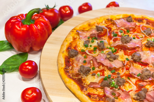 appetizing pizza with bacon, bell pepper and basil on a white table