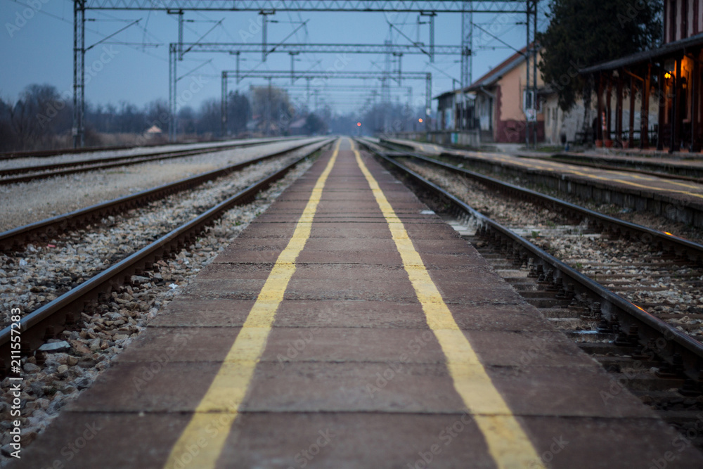 Old train station platform with its distinctive yellow safety lines on an almost abandoned electrified railway line at sunset Old train station platform with its distinctive yellow safety lines on an almost abandoned electrified railway line at sunset