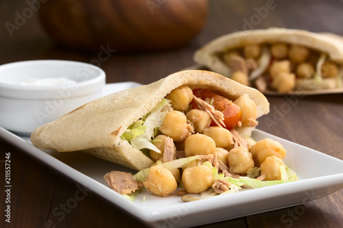 Pita sandwich stuffed with chickpea, tuna, lettuce, pepper, cherry tomato, roasted sunflower seeds on top, photographed with natural light (Selective Focus, Focus one third into the image)