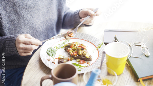 A close up of female hands cutting a tartine of a stew salad on a bread lying on a plate in a cafe