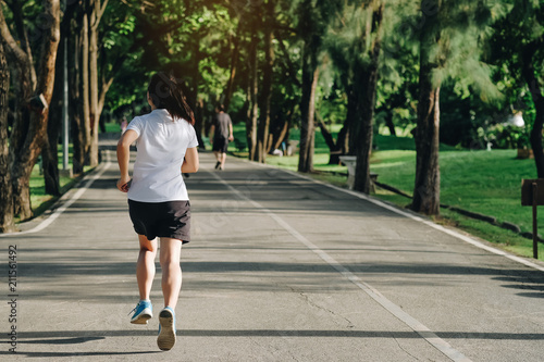 young fitness woman running in the park outdoor, female runner walking on the road outside, asian athlete jogging and exercise on footpath in sunlight morning. Sport, healthy and wellness concepts