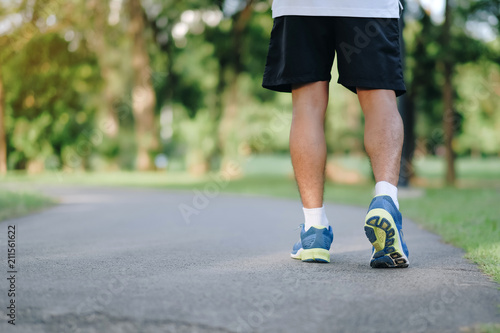 young fitness man legs running in the park outdoor, male runner walking on the road outside, asian athlete jogging and exercise on footpath in sunlight morning. Sport, healthy and wellness concepts