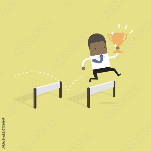 African businessman jumping over obstacle and holding trophy.