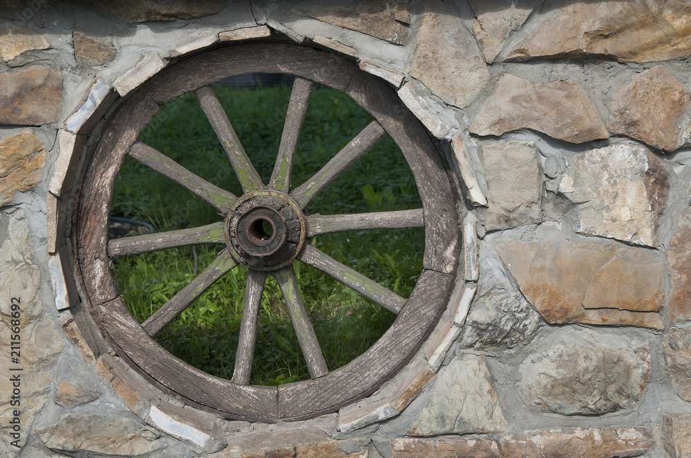 The vintage wheel in the wall made of stones as decoration