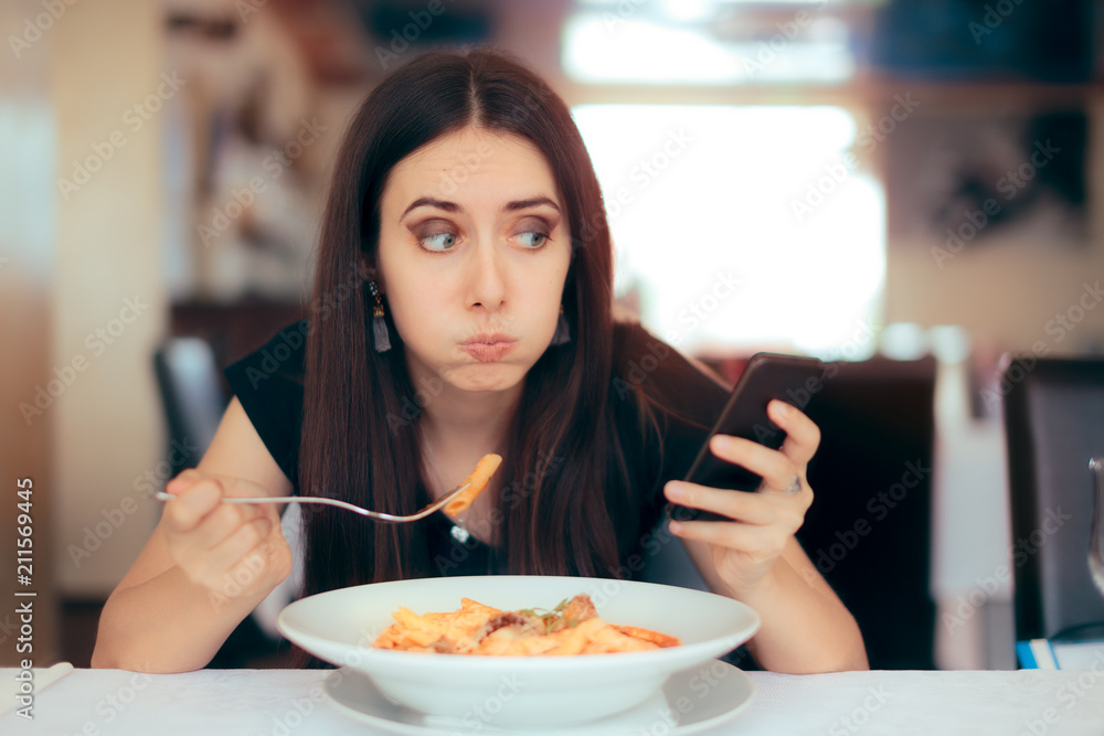 Woman Eating Pasta while Checking her Pone in a Restaurant
