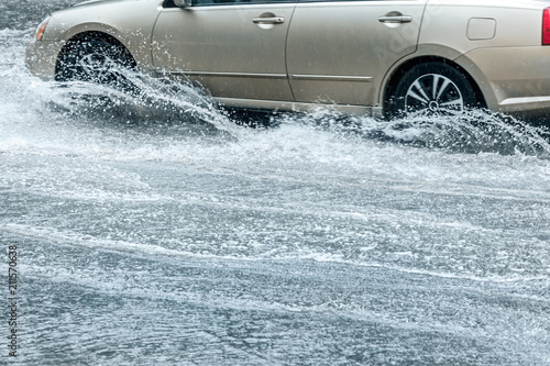 flooded city road with car moving and splashing rain water from wheels