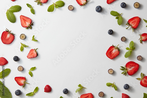 Fototapeta Naklejka Na Ścianę i Meble -  A square frame made of mint leaves, strawberries and blueberries on a gray background. Flat lay