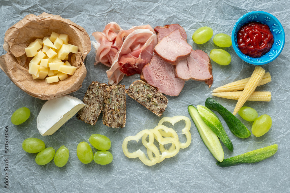 Cold appetizer. Cold cuts. Different snacks on a white crumpled paper, bacon, fruits, grapes, vegetables, from above. Cold appetizer. Cold cuts. Different snacks on a white crumpled paper, bacon, fruits, grapes, vegetables, from above.