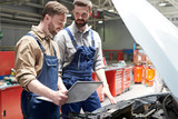 Portrait of two modern bearded mechanics looking under hood of car inspecting engine  while working in car service and repair center, copy space