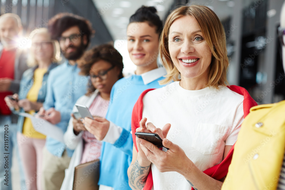 Obraz premium Happy woman in casualwear texting in her smartphone between other people