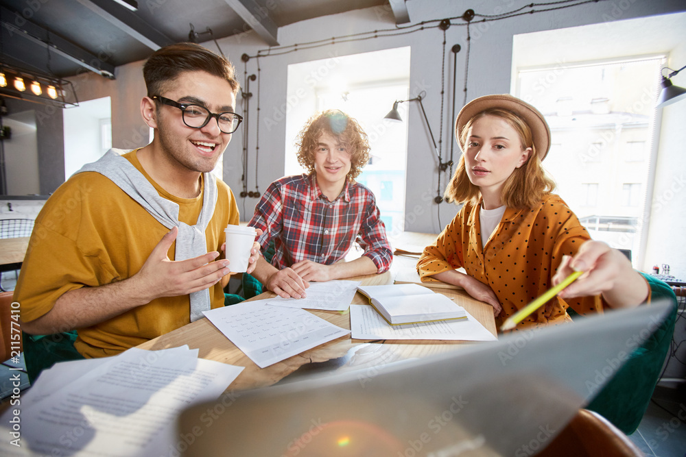 Obraz premium Young businesswoman pointing at data on laptop display while explaining it to colleagues at working meeting