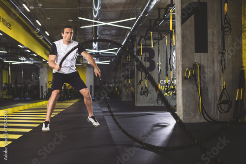 Full length portrait of focused man gesticulating hands with special equipment during exercise in gym © Yakobchuk Olena